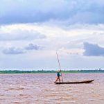 A man standing on a boat in the middle of a body of water